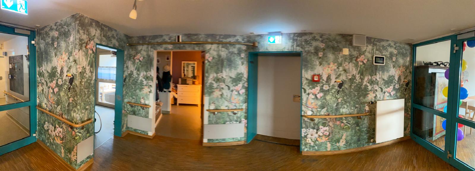 Ein Flur mit einer Tür und einer Wand, die mit dekorativem Tapetenmuster gestaltet ist.